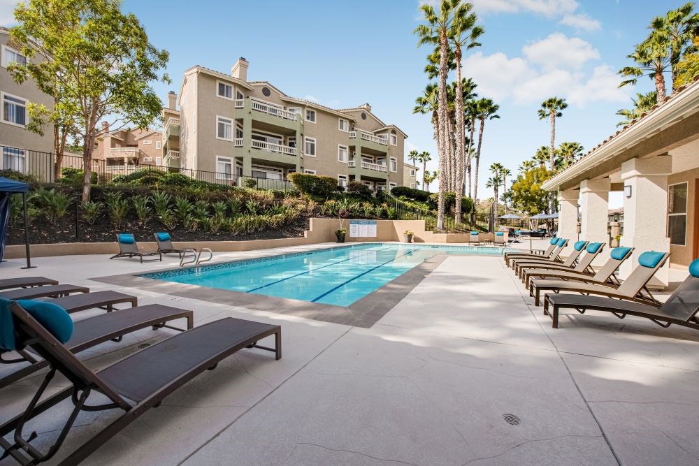 A pool area with sun loungers and a building in the background.