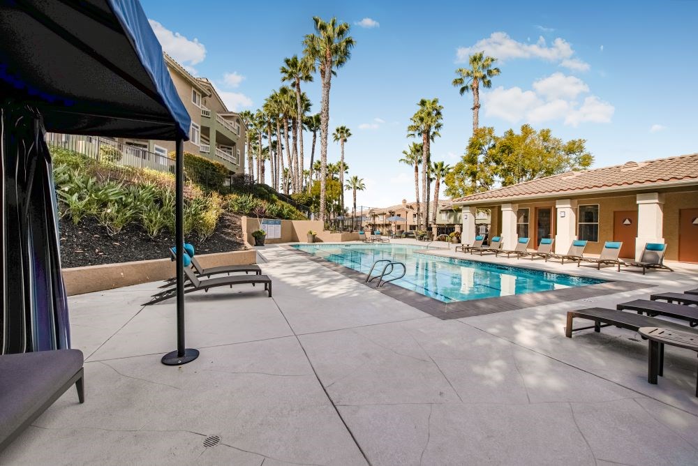 A pool area with a black umbrella and lounge chairs.