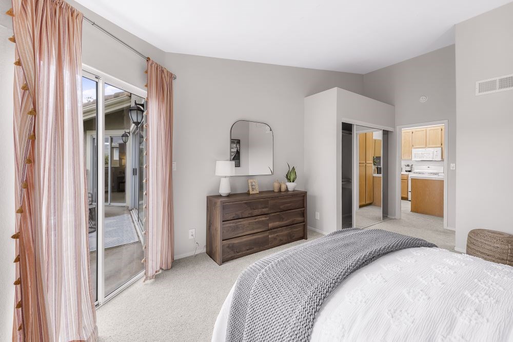 A bedroom with a large bed, a dresser, and a sliding glass door.