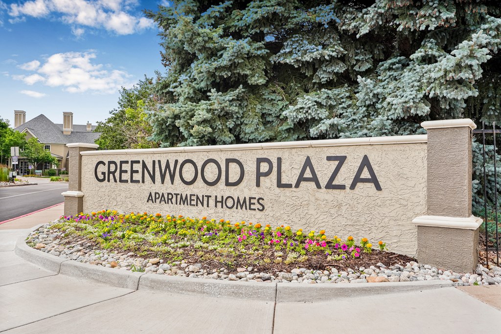 A sign for Greenwood Plaza Apartment Homes is surrounded by flowers.