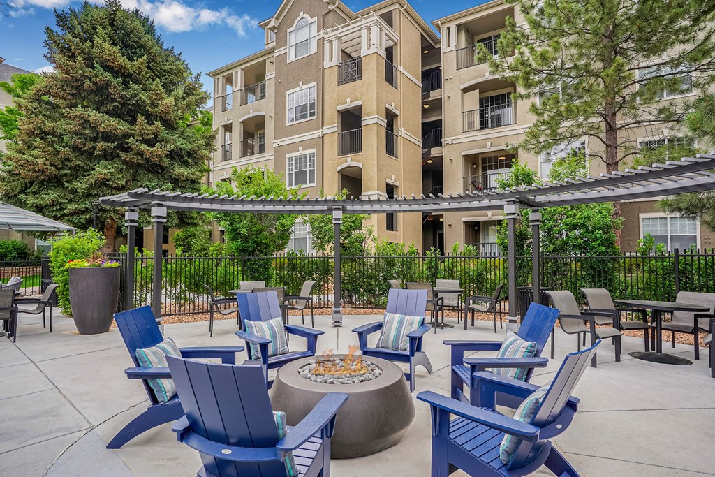 A patio with blue chairs and a fire pit in front of a building.