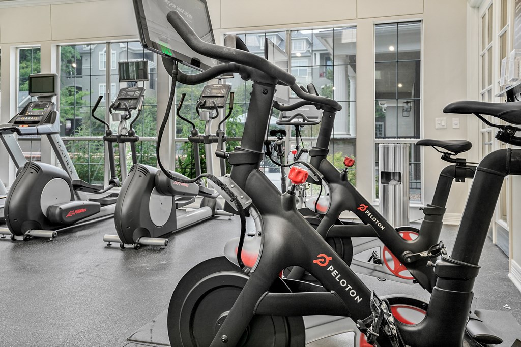 A Peloton bike is in the foreground of a gym with other exercise bikes in the background.