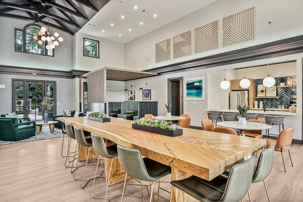 A long wooden table with chairs is in the middle of a room with a green couch and a plant on the table.