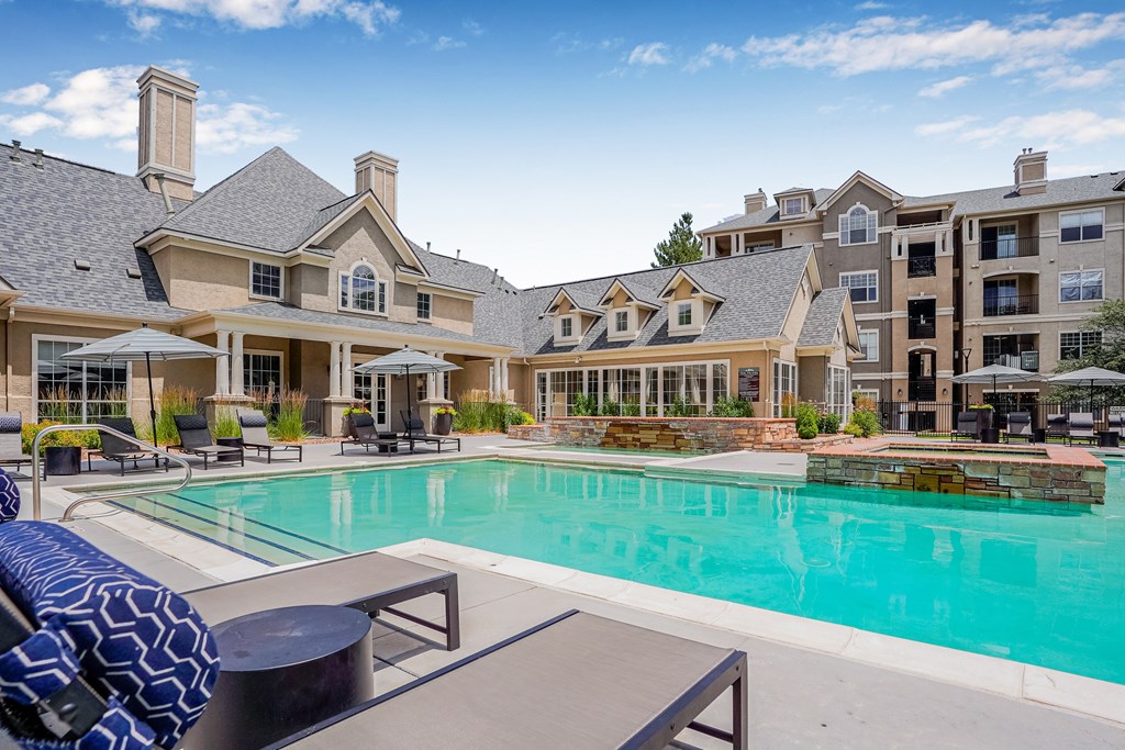 A large swimming pool in front of a building with a blue umbrella.