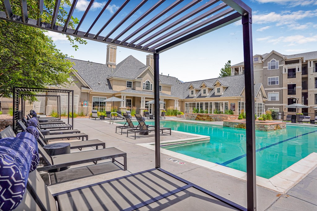 A pool area with a shaded seating area and a building in the background.