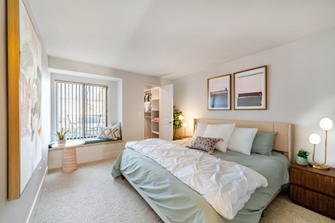A bedroom with a bed, nightstand, and a window with a view of a balcony.