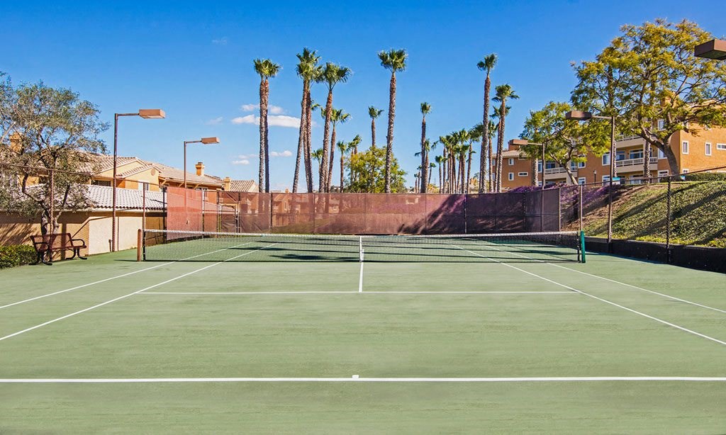 a tennis court with palm trees and buildings in the background
