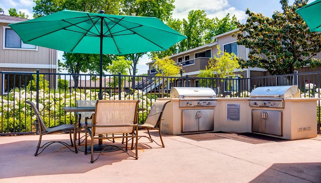 a patio with two bbqs and a table with chairs and an umbrella