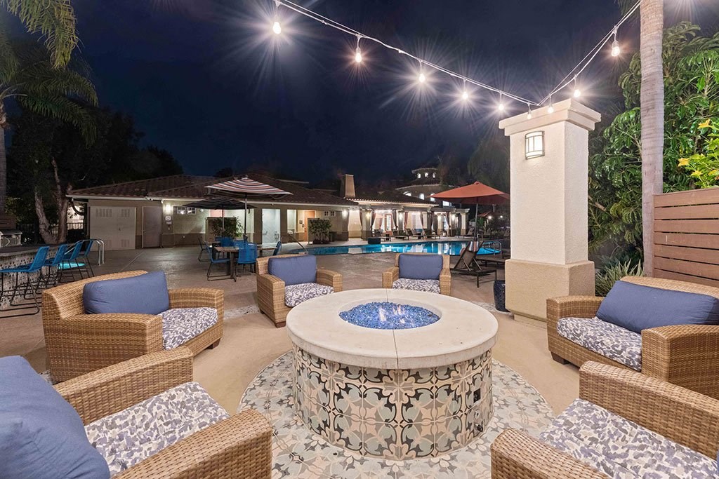 a patio with a fire pit and chairs and a pool at night
