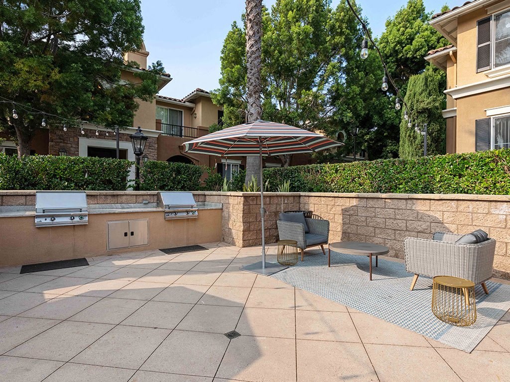 a patio with a grill and chairs and an umbrella