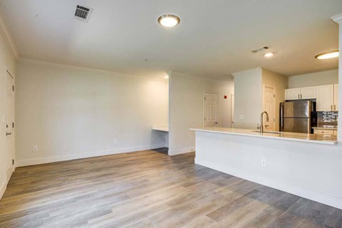 an empty living room with a kitchen and a refrigerator