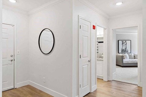 a white hallway with a mirror on the wall and a door to a living room