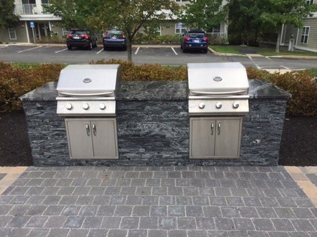two stainless steel barbecue grills on a stone counter in a driveway
