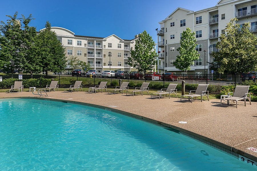 a swimming pool with chairs in front of an apartment building