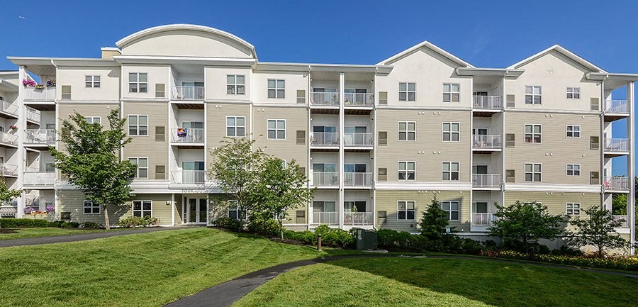 an apartment building with a green lawn and trees