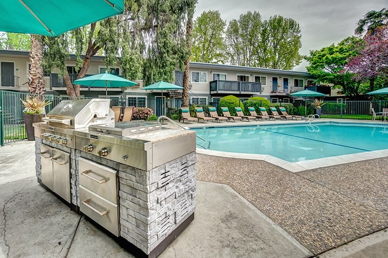 a grill next to a swimming pool with umbrellas