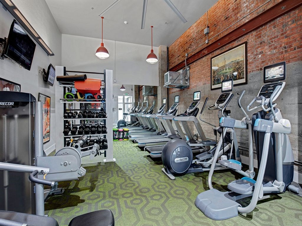 a gym with cardio equipment and weights on the wall