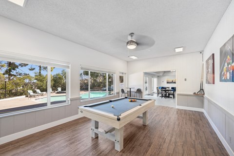 a game room with a pool table and a view of a pool house with windows