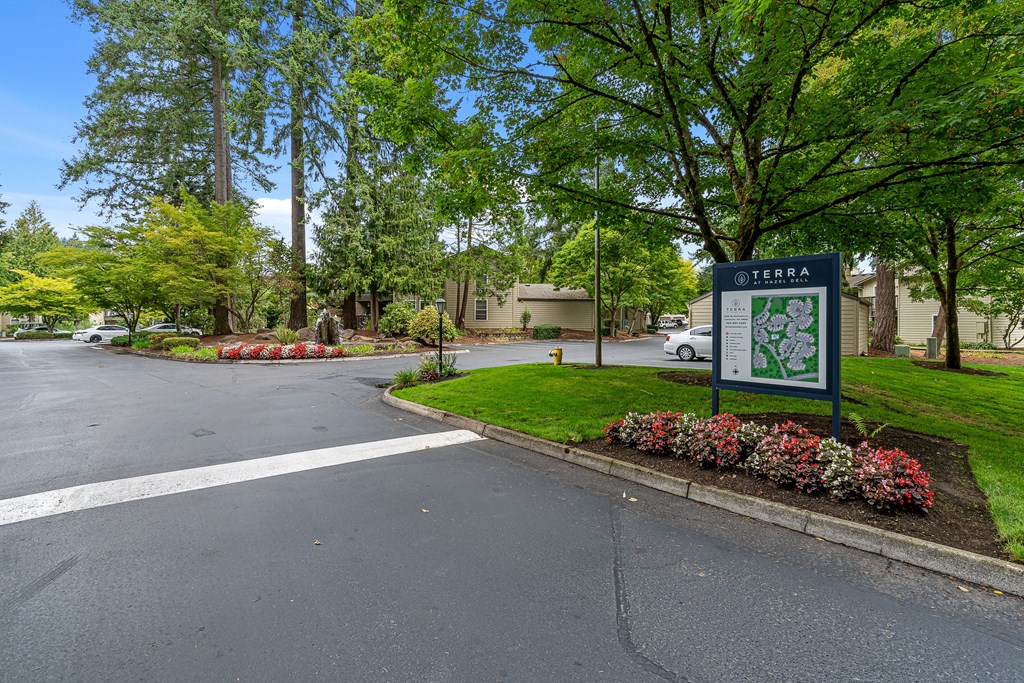 a sign in front of a road with trees and a building in the background