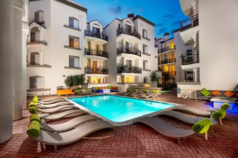 A swimming pool surrounded by lounge chairs in front of apartment buildings.
