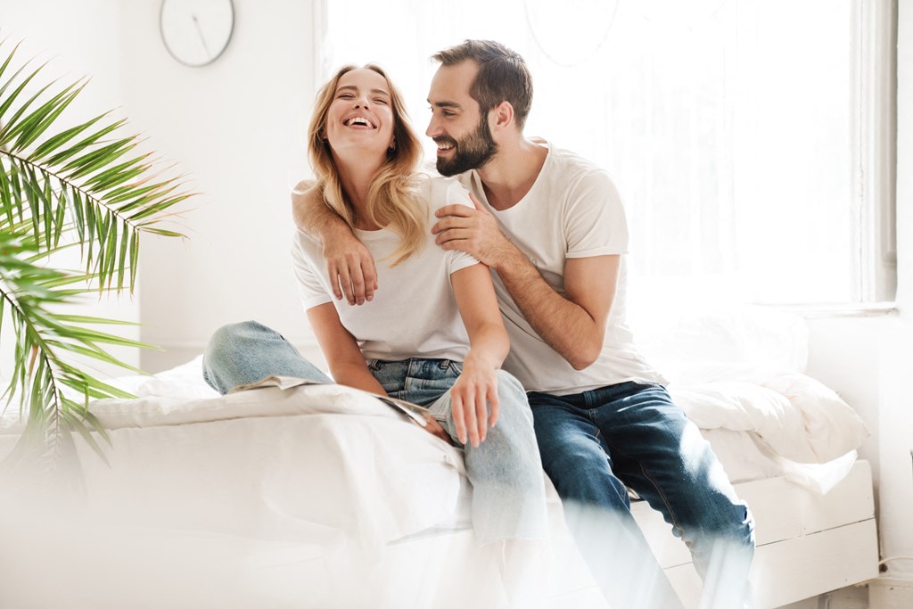 a man and a woman sitting on a bed laughing