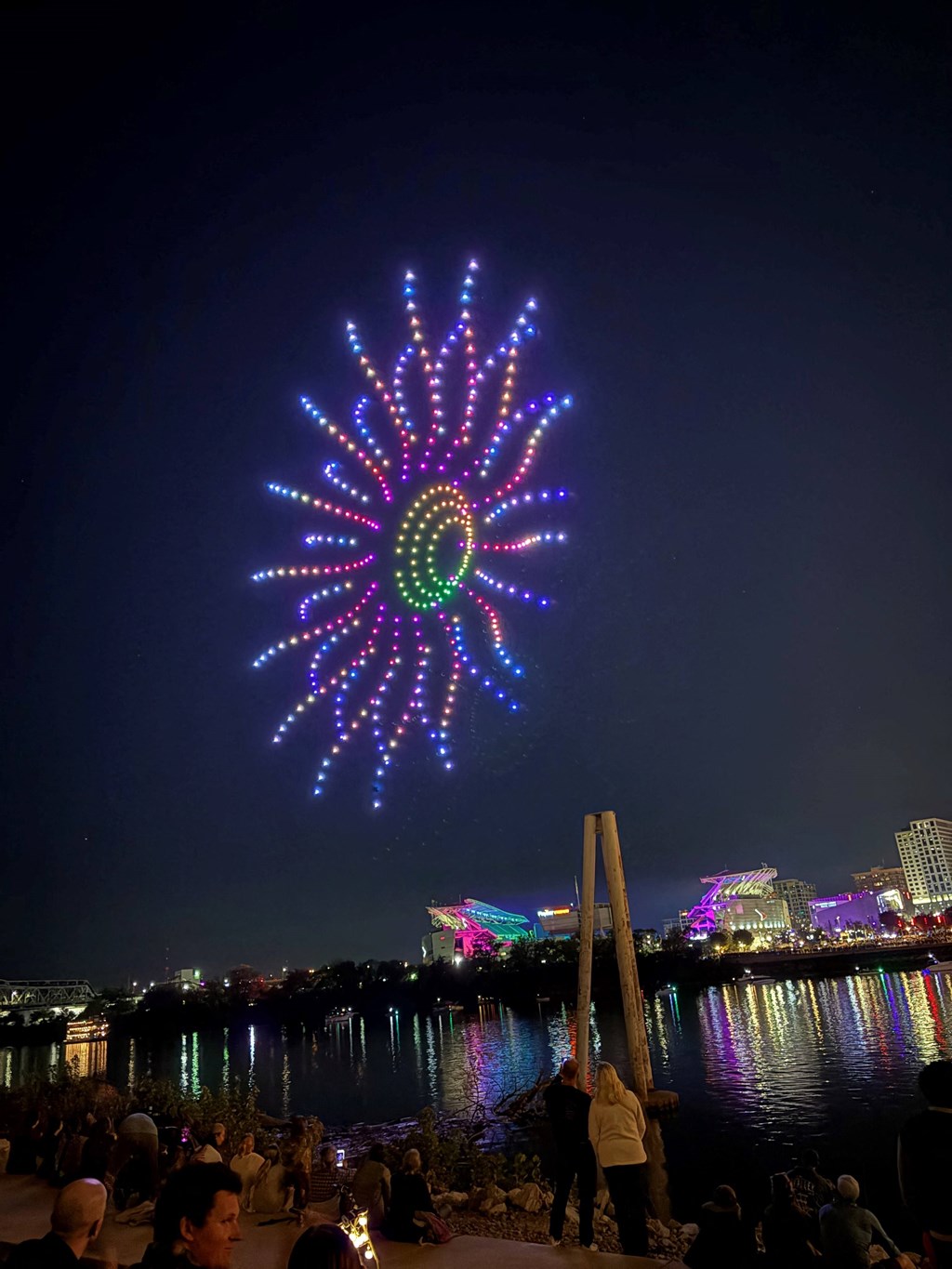 A firework display over a body of water with people watching.