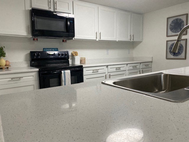 A kitchen with white cabinets and a black microwave above the stove.