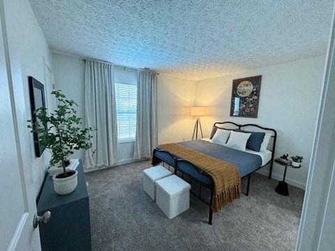 A bedroom with a bed, nightstand, and a potted plant.