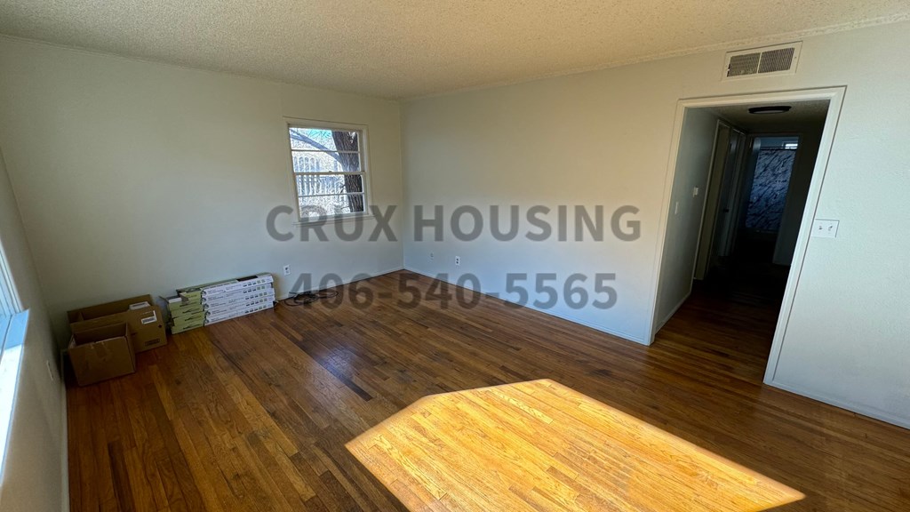 A room with wooden flooring and a white wall with the text "CRUX HOUSING" and a phone number.