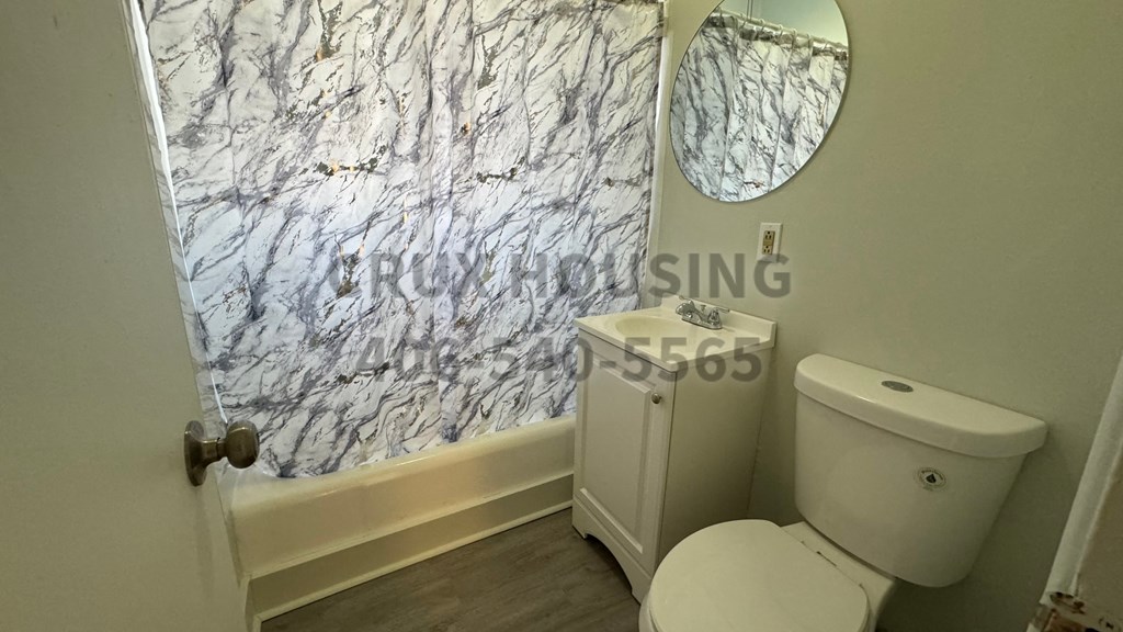 A bathroom with a toilet, sink, and a marble wallpapered shower.