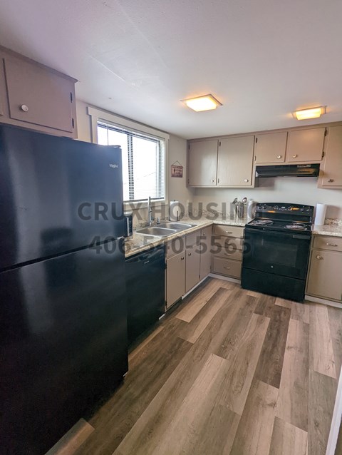 A kitchen with a black fridge and wooden floors.