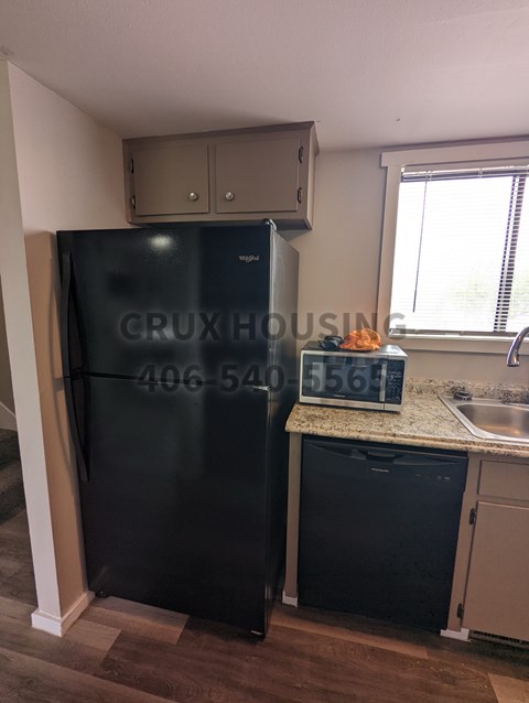 A kitchen with a black fridge and a window with blinds.