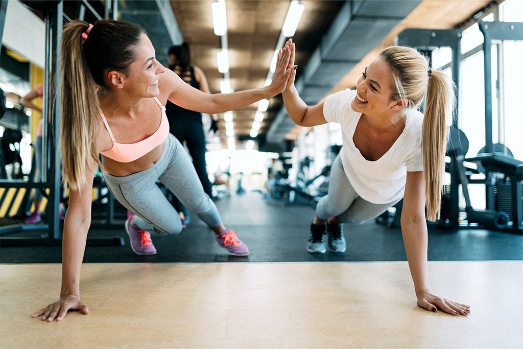 two women giving each other a high five while doing push ups in the gym at Morea Apartments, Pompano Beach, Florida