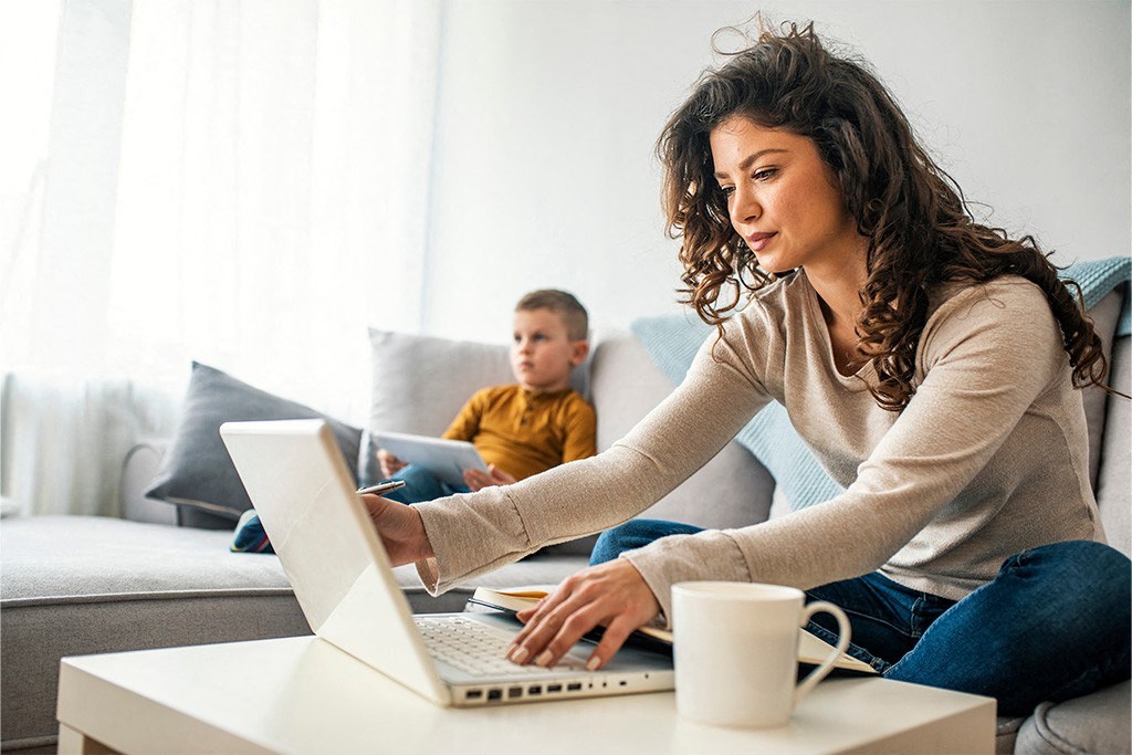 a woman working on a laptop while a boy sits on a couch in the background at Morea Apartments, Pompano Beach, 33062