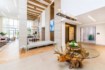 Clubhouse with a glass coffee table and a large window. at Morea Apartments, Pompano Beach, 33062