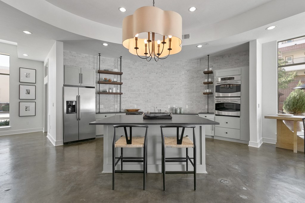 a kitchen with a large island with two stools and a stainless steel refrigerator
