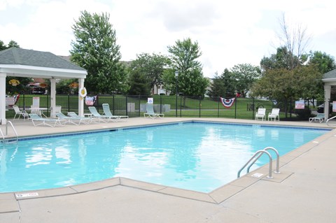 A pool with a gazebo and chairs around it.