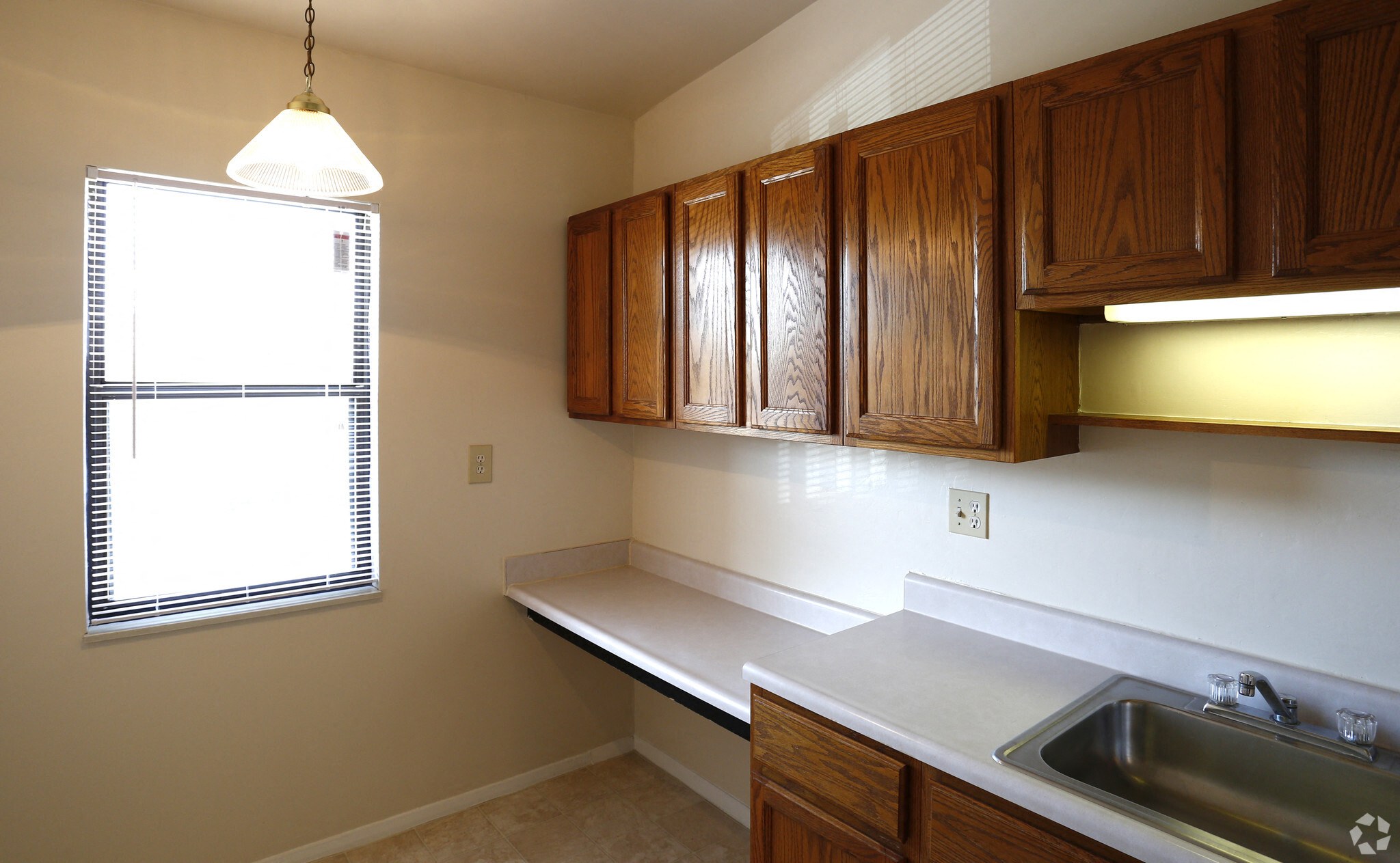 A kitchen with wooden cabinets and a window with blinds.
