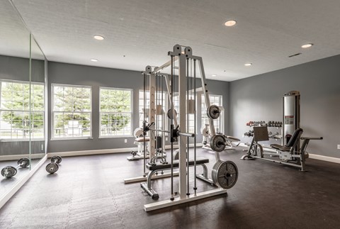 A spacious gym with a variety of equipment including a squat rack, bench press, and dumbbells at Twin Fountains Apartments, Mason, OH