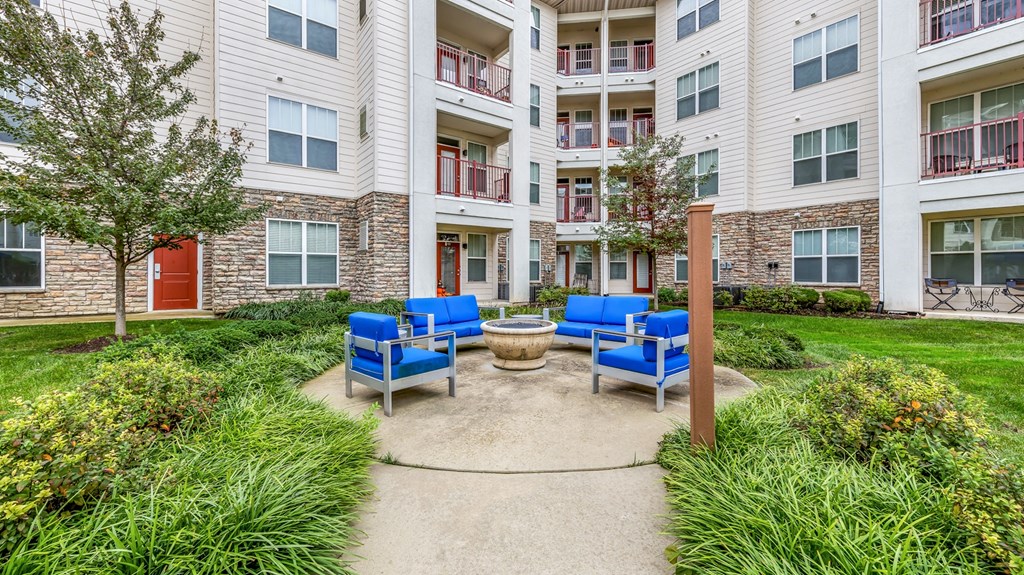 an outdoor patio with blue chairs and a fire pit in front of an apartment building at Vanguard Crossing, St. Louis, Missouri