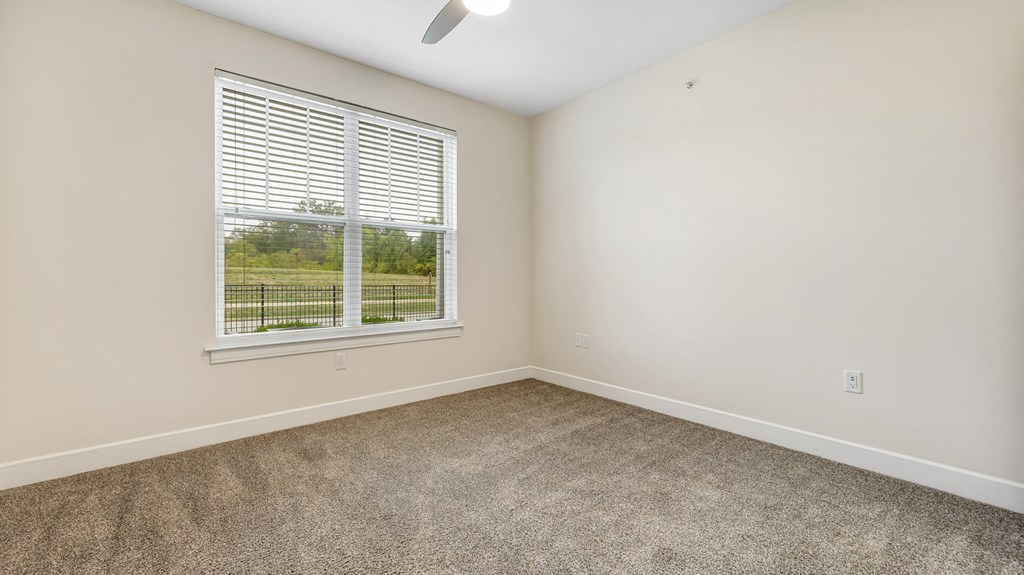 an empty bedroom with a window and carpeting at Vanguard Crossing, St. Louis, MO