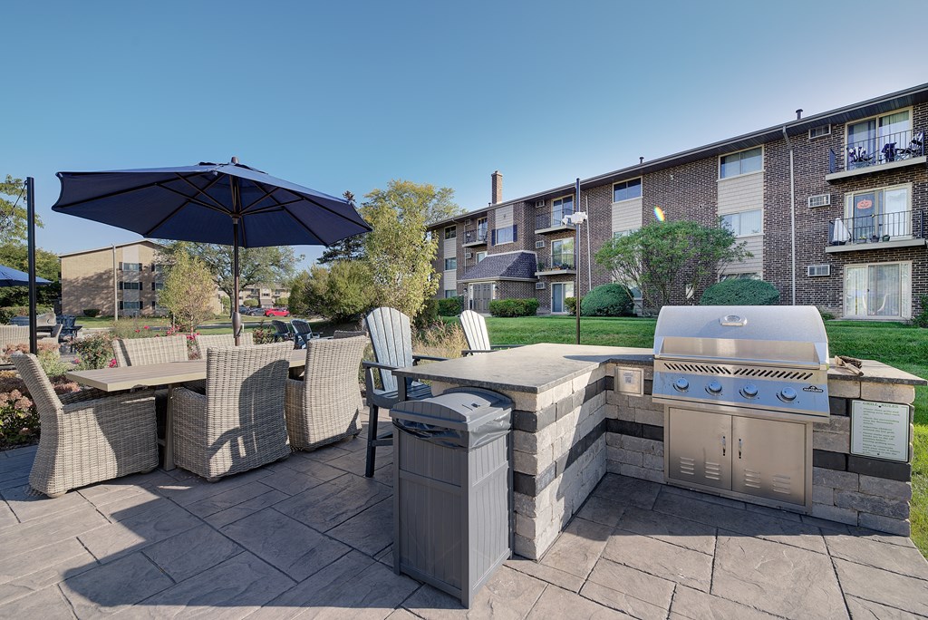 a backyard with an outdoor grill and table with chairs and an umbrella at The Greenway at Carol Stream, Illinois