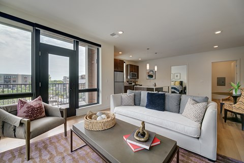A modern living room with a white sofa and a glass door leading to a balcony.