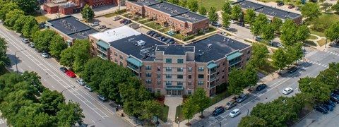 A large red brick building with a green roof is surrounded by trees and a parking lot.