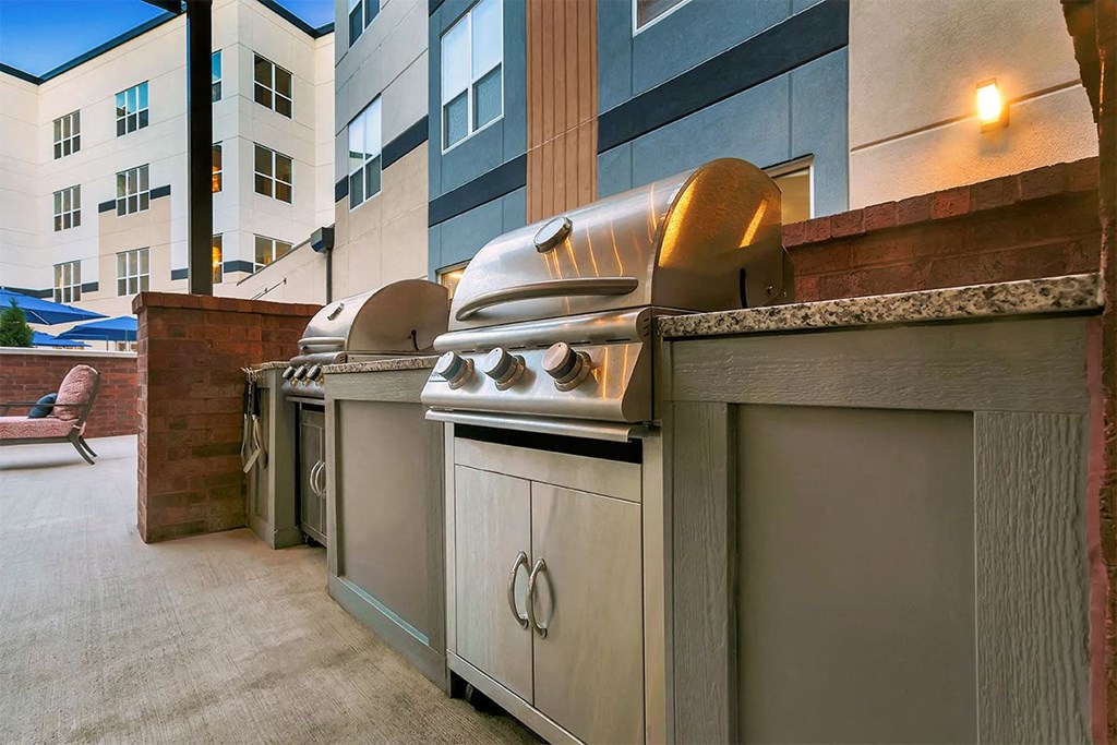 a row of barbecue grills on a patio next to a building at Aster Apartments, Beachwood Ohio