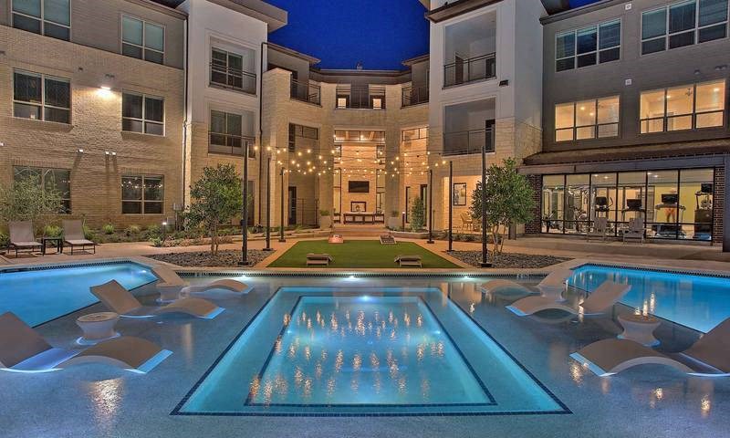 a swimming pool with chairs in front of an apartment building at Hunters Creek Apartments, Texas