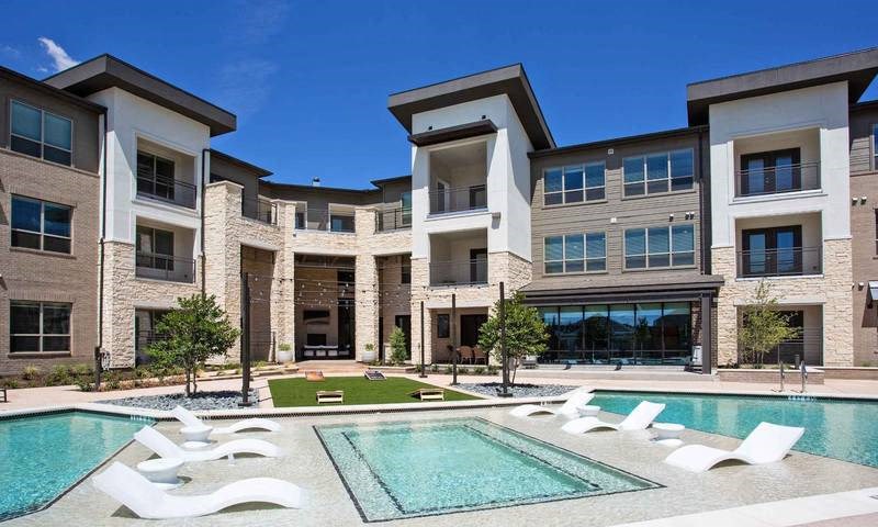 a pool with white chairs in front of an apartment building at Hunters Creek Apartments, Denton Texas