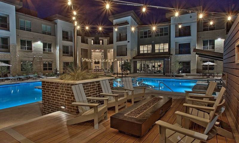 a swimming pool with rocking chairs in front of an apartment building at Hunters Creek Apartments, Denton Texas