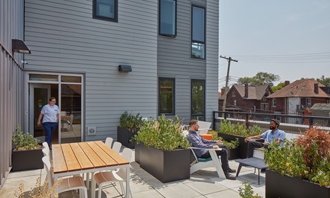 Two men are sitting on chairs and talking in a patio area.