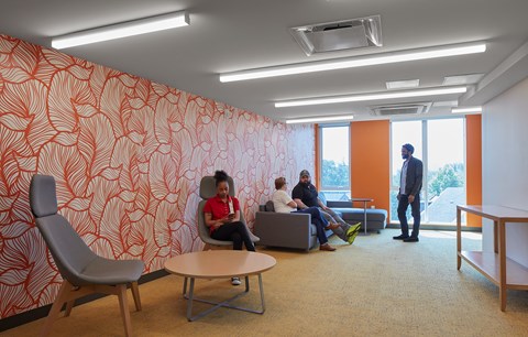 A group of people are sitting in a room with orange wallpaper.